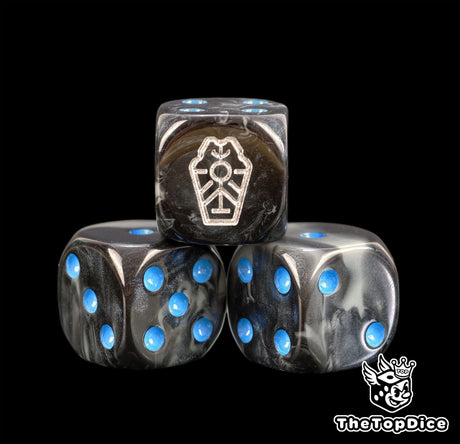 Close up of three blue Necron dice, black grey marbled resin with a silver dynasty glyph and blue pips