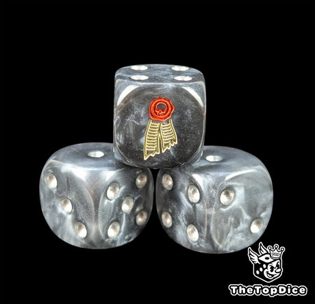 Close up of a black 16mm resin D6 die engraved with a beige scroll and red wax seal and silver pips