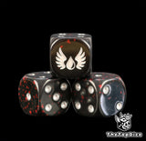 Close up of three Blood Angels dice, black resin splattered red with a white winged blood drop and silver pips