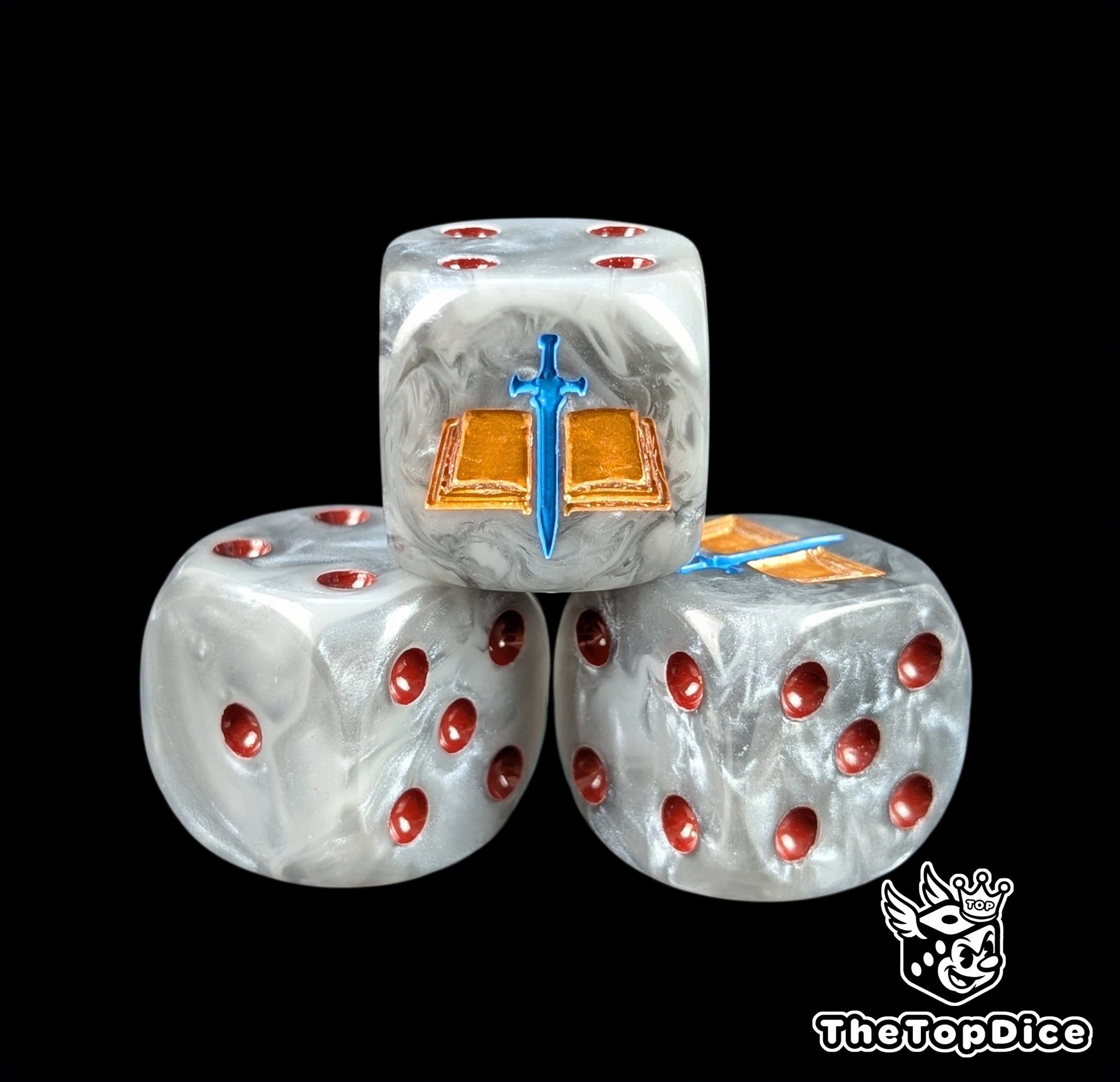 Close up of a grey 16mm resin D6 die engraved with a gold tome and blue blade and red pips