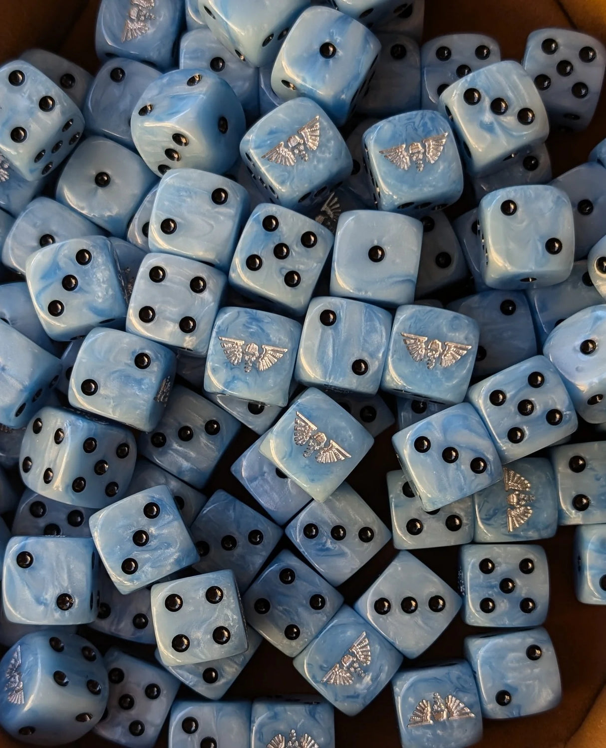 Pile of sky blue 16mm D6 dice with silver winged helms for a sci-fi trench army
