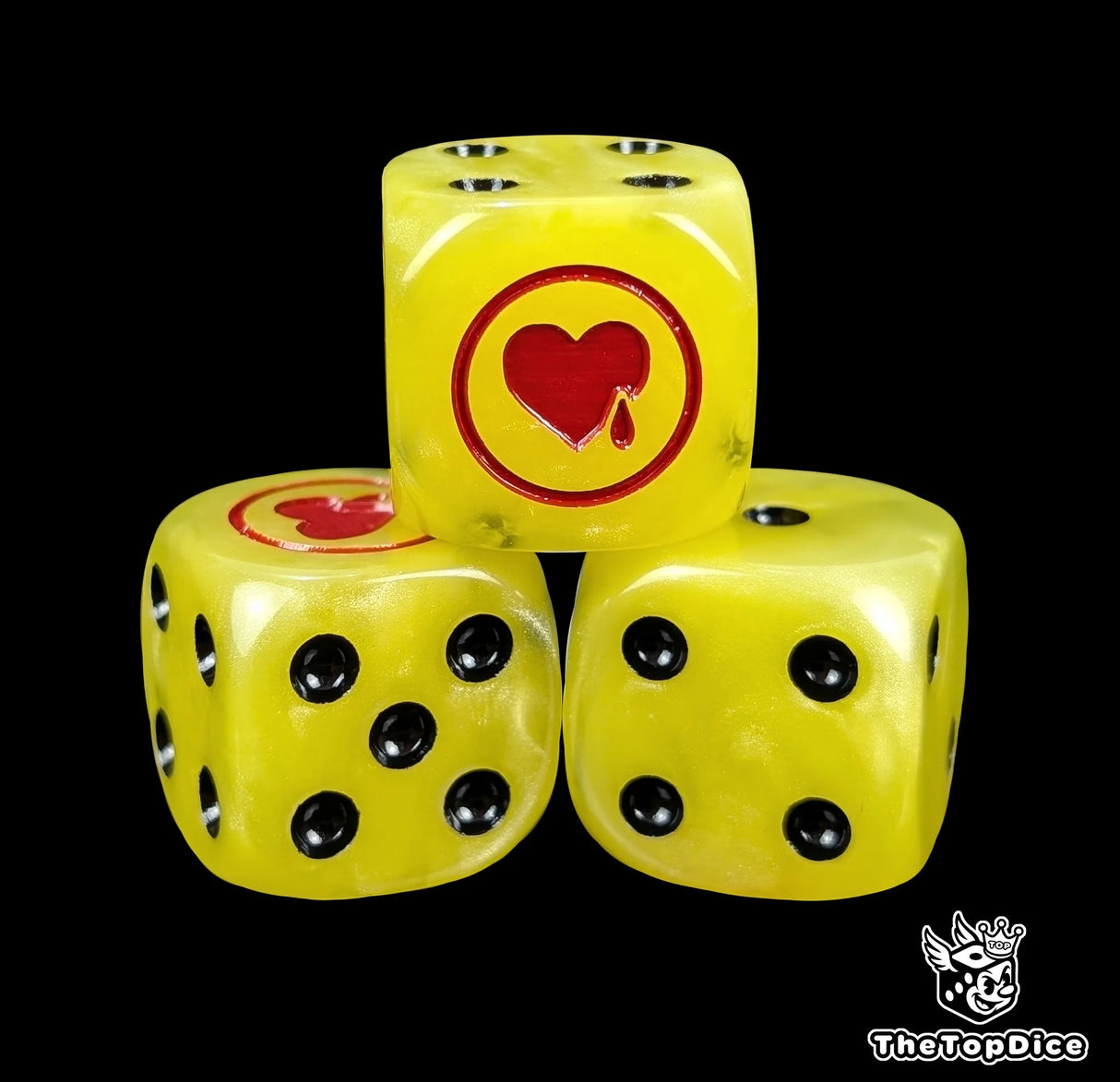 Close-up of three yellow 16mm grimdark D6 dice engraved with a red heart emblem
