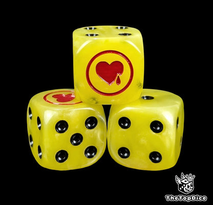 Close-up of three yellow 16mm grimdark D6 dice engraved with a red heart emblem