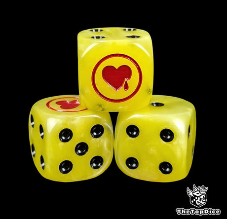 Close-up of three yellow 16mm grimdark D6 dice engraved with a red heart emblem