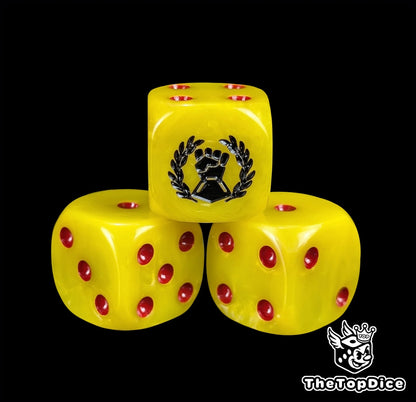 Close up of a yellow 16mm resin D6 die engraved with a black fist and laurel and red pips